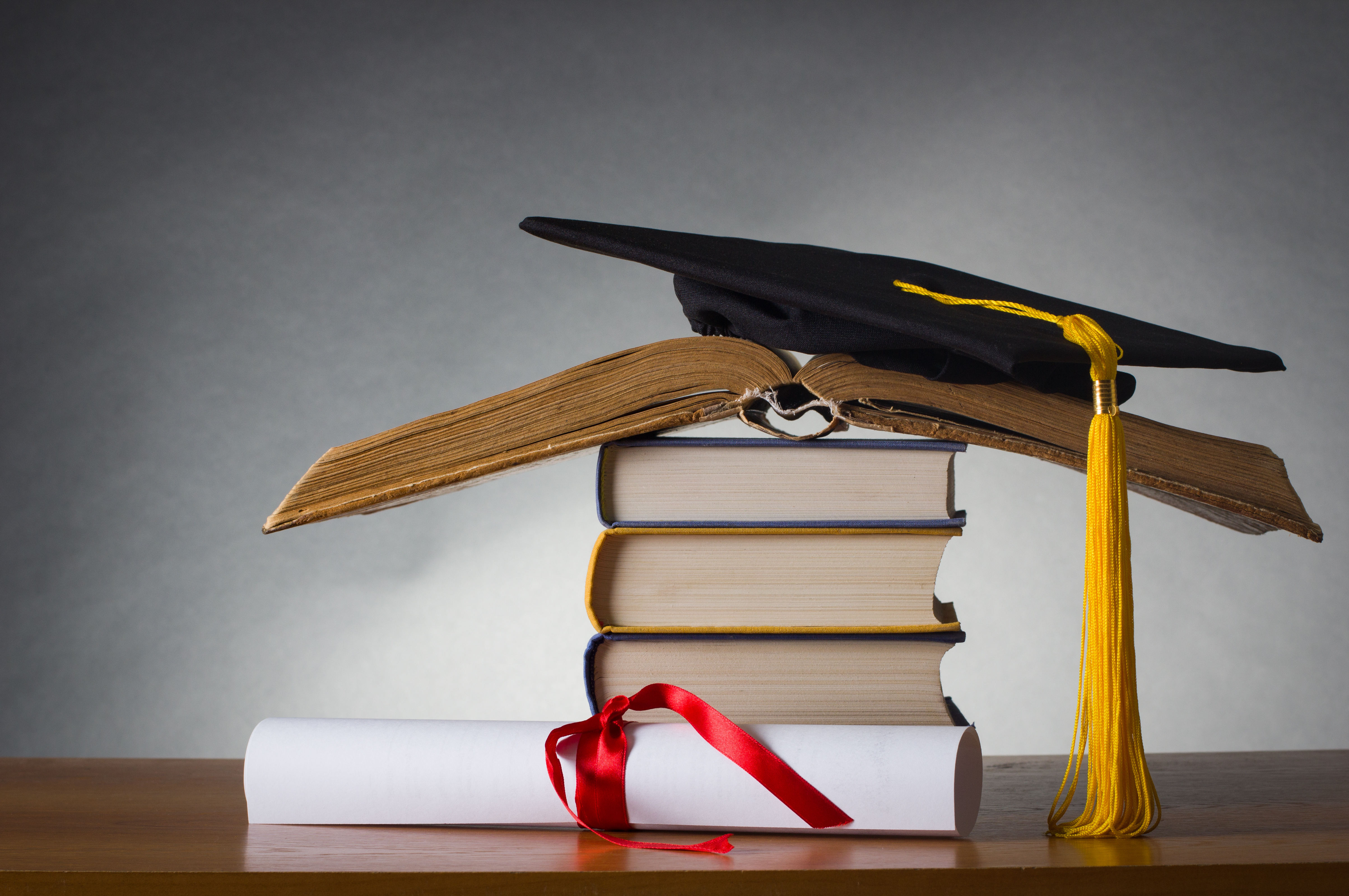 mortarboard and graduation scroll on a stack of battered book